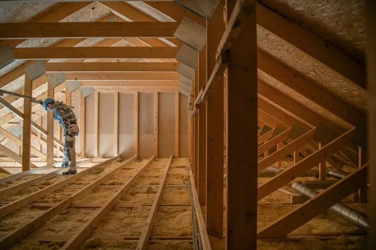 Attic construction featuring a worker inspecting wooden roof framing and insulation, emphasizing the importance of proper HVAC installation for efficient indoor climate control in commercial buildings.