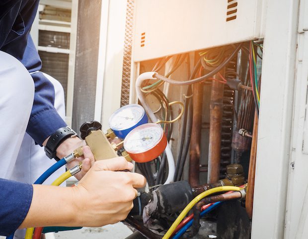 HVAC technician using pressure gauges on air conditioning unit for maintenance and repair services in Dallas, TX.