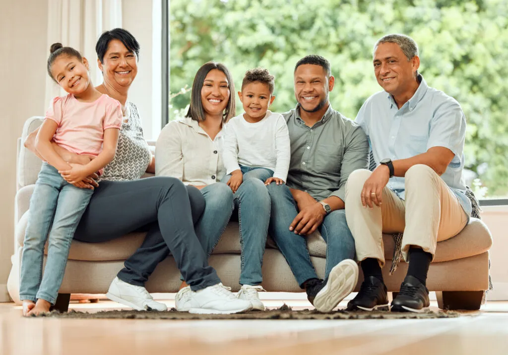 Family portrait with grandparents and children sitting together on a couch, smiling, in a well-lit living room, emphasizing warmth and togetherness.