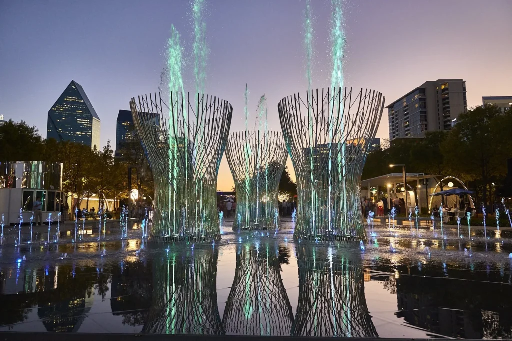 Dallas, TX: Water fountain art installation at a park with buildings in the background. Heat Pump Repair may be needed in nearby buildings.