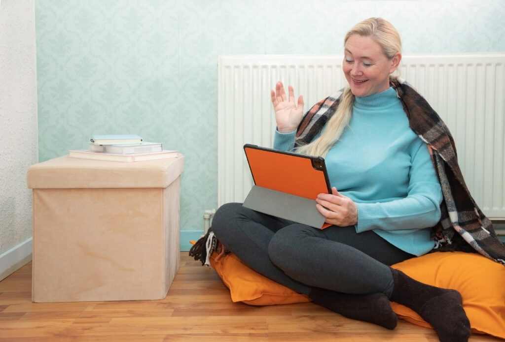Woman at home wrapped in a warm blanket, using a tablet and smiling, with a cozy setting highlighting comfort and warmth, relevant to furnace repair services in Dallas, TX.