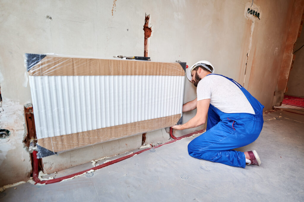 Man installing new heating system. Radiator installation with red pipes. Heating installation services.