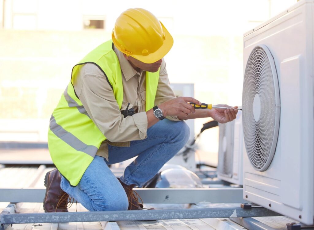 Air conditioning technician in safety gear working on heat pump installation on a rooftop in Dallas, TX.