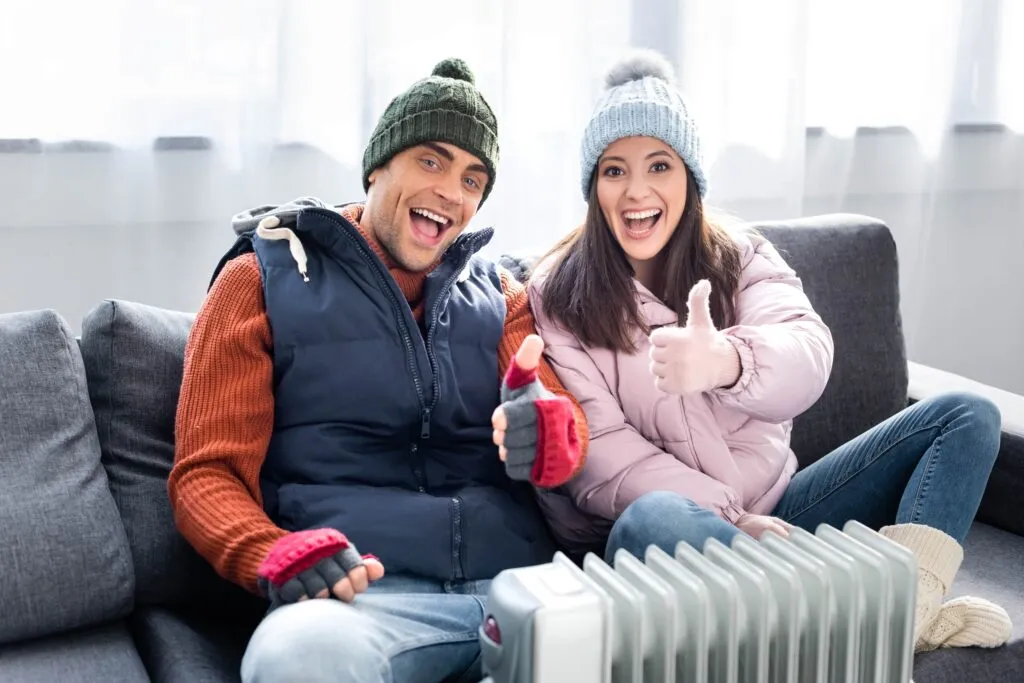 Happy couple with heater giving thumbs up. Heating repair may be needed if your heater isn't working. Stay warm in Dallas, TX.