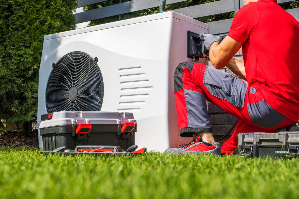 Technician in red uniform performing maintenance on a heat pump unit in a residential yard, surrounded by tools and equipment, emphasizing HVAC repair services in Dallas, TX.