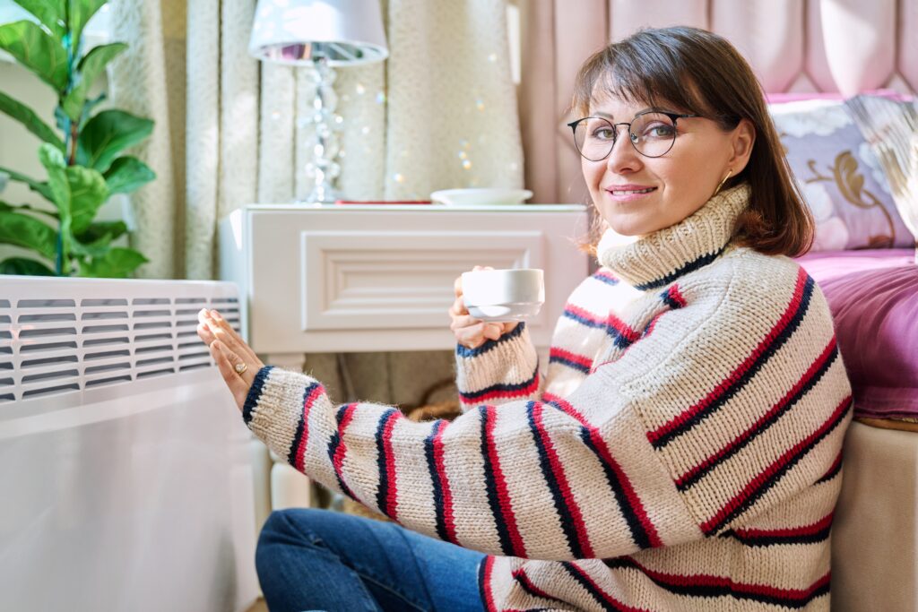 Woman warming hands by heater. Heating Installation for your home in Dallas, TX. Stay warm with our heating services.