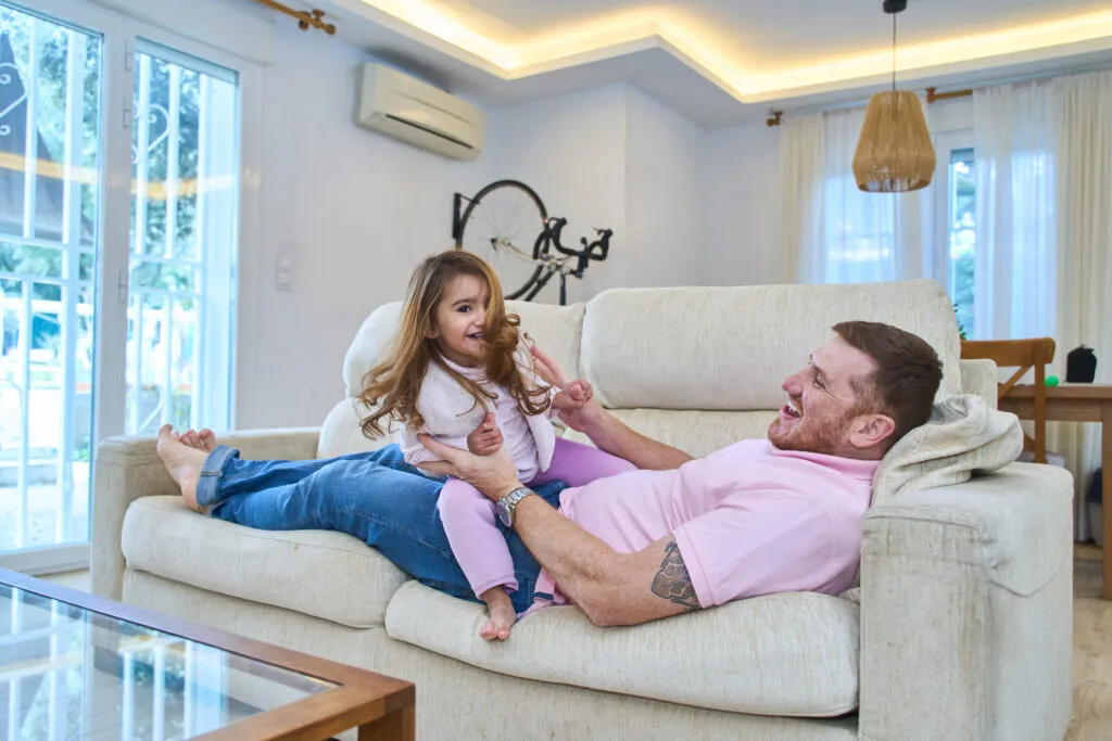 Father and daughter relax under a mini-split system. Consider Ductless Mini-Split Repair for optimal comfort in Dallas, TX.