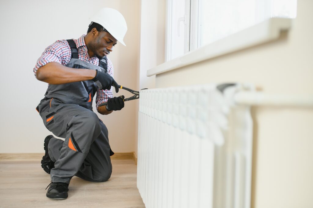 Man in workwear overalls and safety helmet performing maintenance on a radiator, showcasing expert heating service for efficient home warmth.