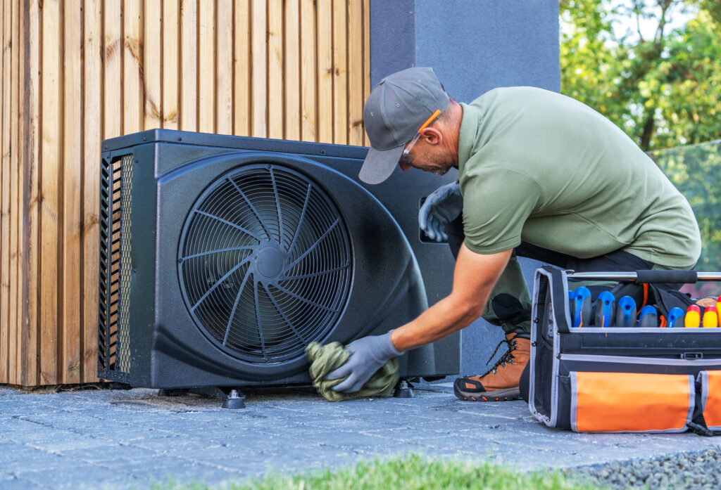 Technician performing heat pump maintenance. Man cleaning outdoor AC unit with toolbox nearby. Dallas, TX HVAC service.