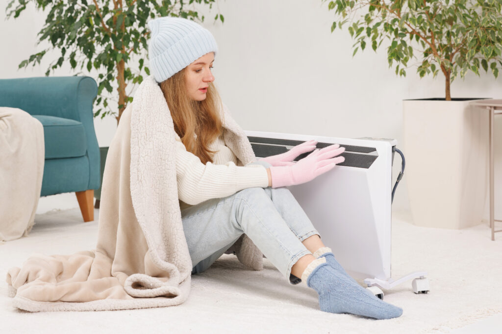 Woman in winter clothes near heater, illustrating home heating maintenance in Dallas.