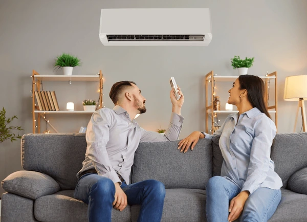 Happy couple relaxing on a sofa under an air conditioning unit, enjoying improved indoor air quality and comfort in a stylish living room.