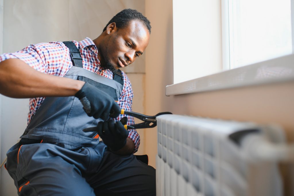Repairman in overalls using tools to service a radiator, highlighting emergency heating repair services in Dallas, TX.
