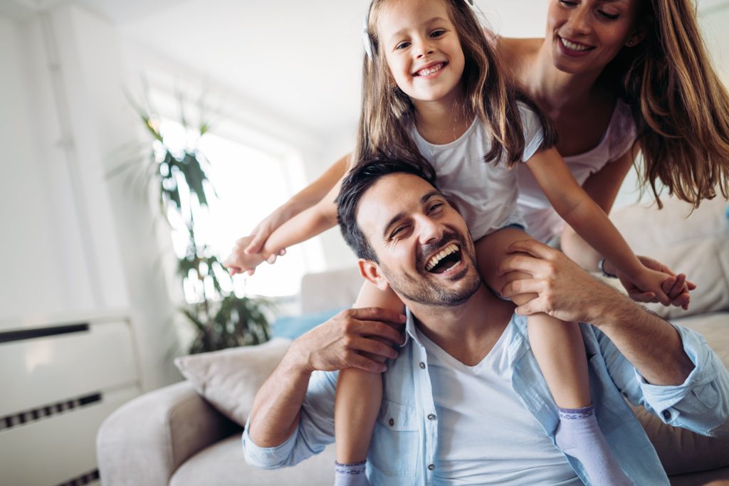 Happy family with programmable thermostat in a cozy home. Father carrying his daughter on his shoulders, mother standing behind them smiling.