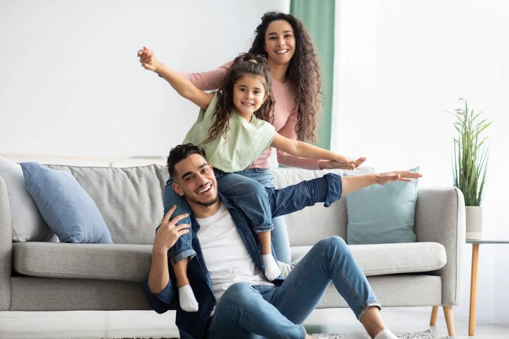 Happy Middle Eastern family enjoying quality time at home, with parents bonding and playing with their daughter in a cozy living room setting.