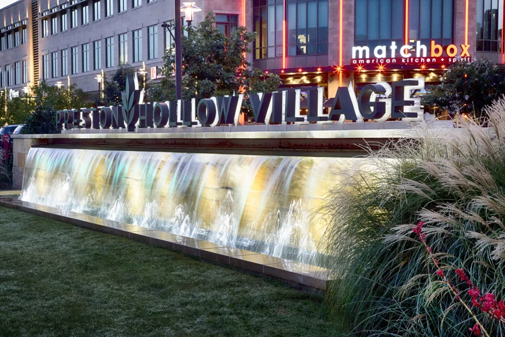 Entrance sign for Preston Hollow Village in Dallas, TX, with a unique water feature in front. A vibrant community hub and shopping destination.