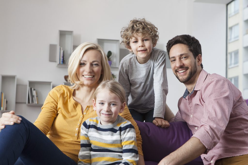 A happy family of four in Park Cities, Dallas, TX, smiles for a photo. The mother, father, and two children are casually dressed and relaxed.