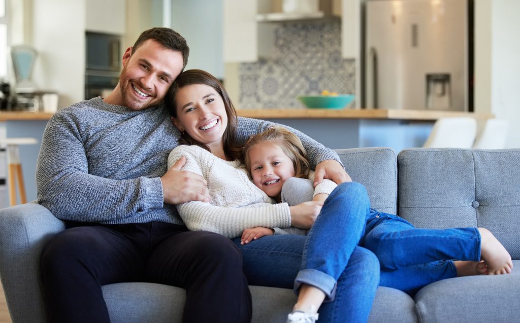 Young family relaxing together on a couch, enjoying quality time in a cozy living room, symbolizing comfort and warmth associated with reliable heating services.
