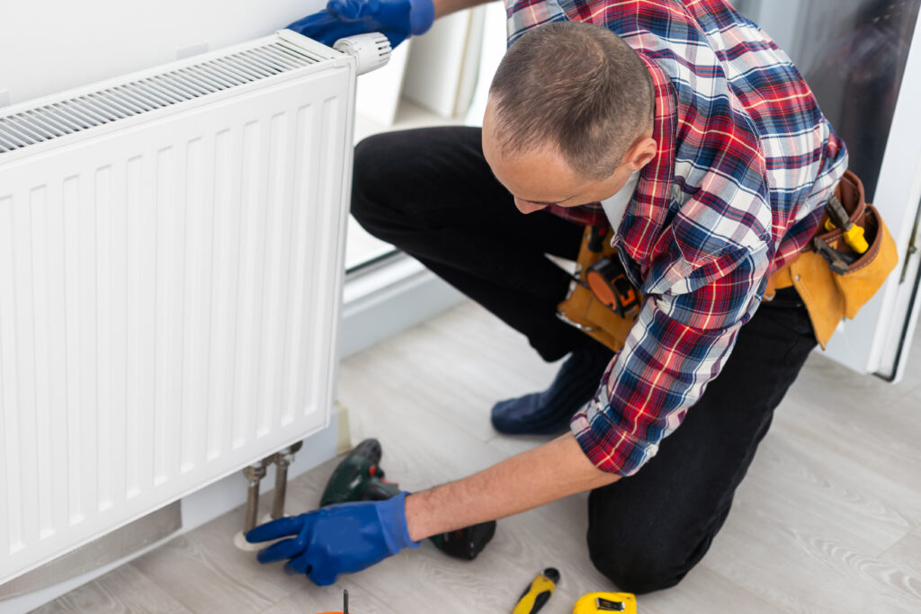 Technician installing baseboard heating radiator, emphasizing HVAC expertise and home comfort solutions in Dallas, TX.