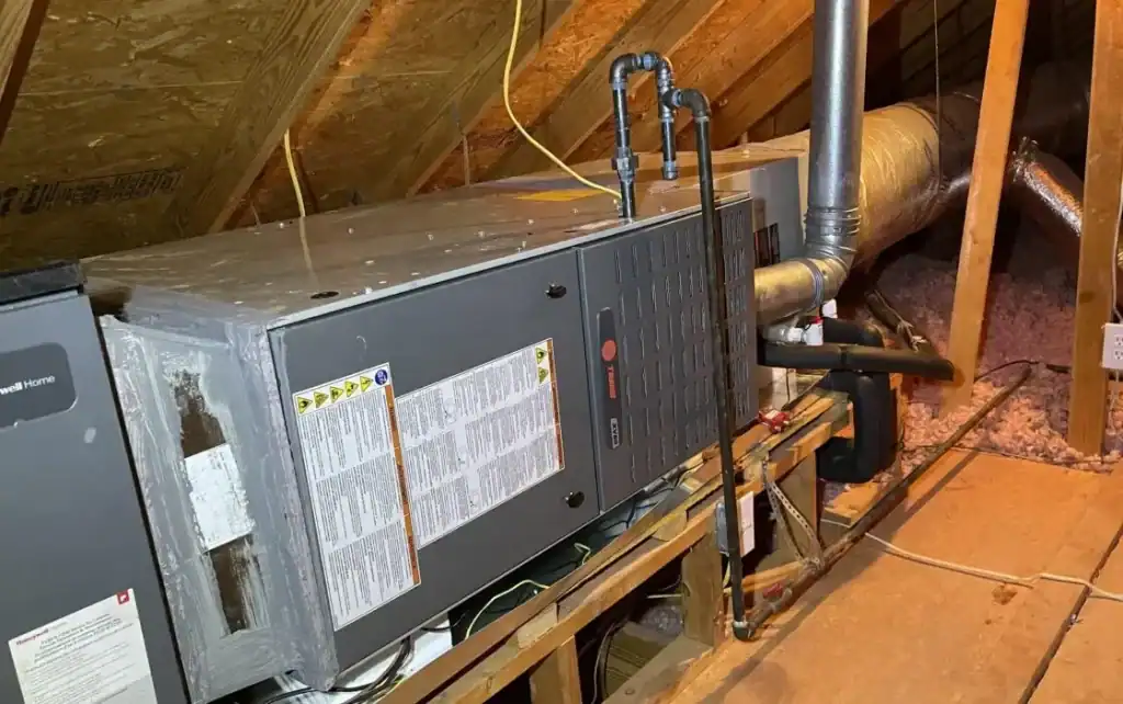 A Trane air handler unit installed in a residential attic space with metal ductwork and piping visible in the rafters of a home.