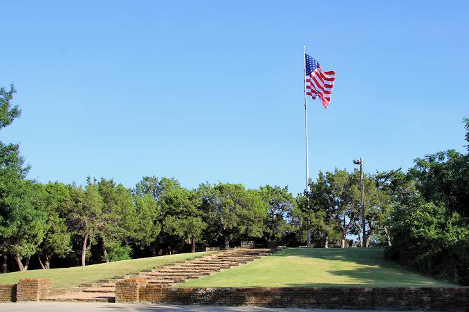 American flag flies on a tall pole above a brick staircase and grassy hillside in a scenic park area of Lake Highlands Dallas TX